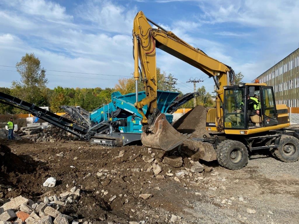 Rypadlo CAT plní hrubotřídič Powerscreen Warrior 800